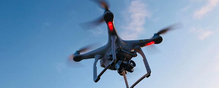 Black drone flying in a blue sky with just a few scattered clouds